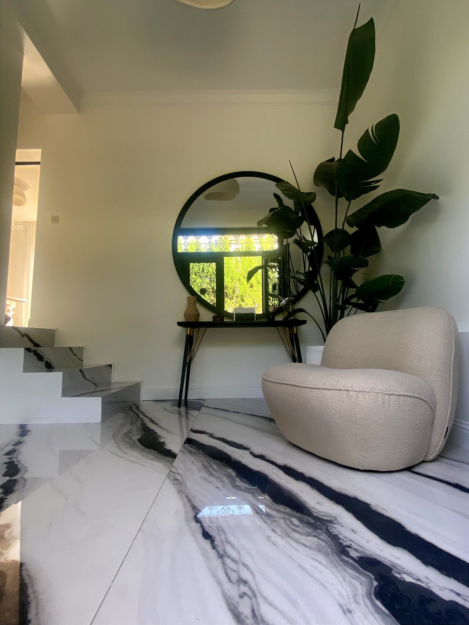 Fauteuil Fontaine en tissu bouclette beige Paname Avenue dans une entrée contemporaine avec sol effet marbre, miroir rond et plante XXL - retour client