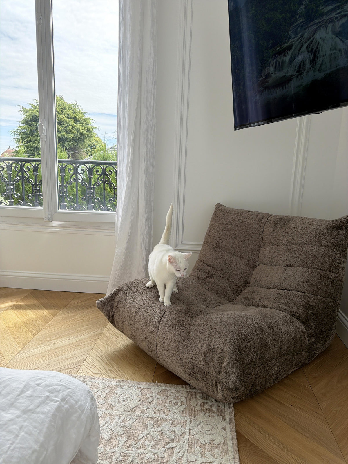 Fauteuil Moret en tissu chenille taupe de chez Paname Avenue dans une chambre lumineuse avec parquet chevron et fenêtre haussmannienne - retour client