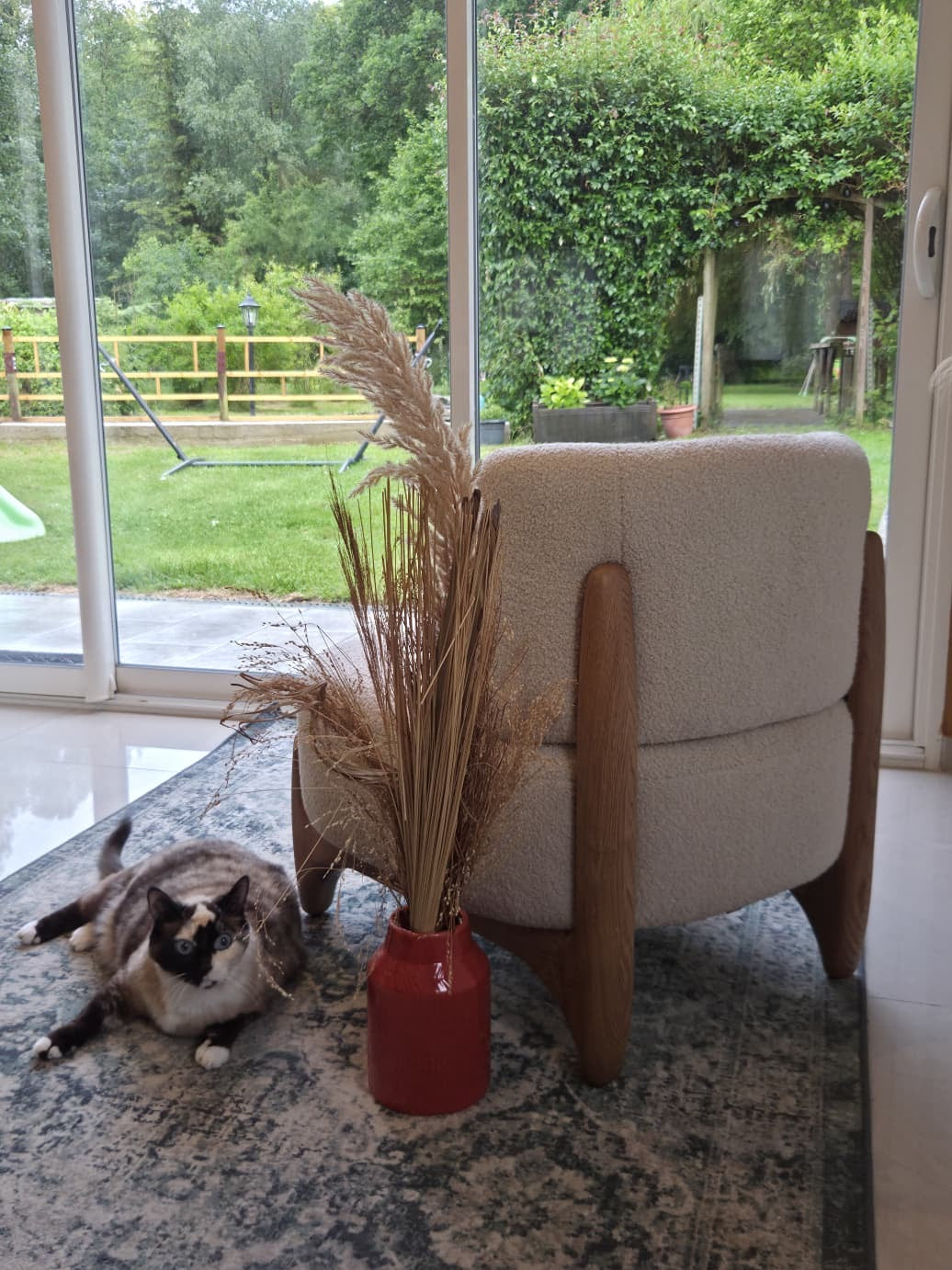Fauteuil Rivoli en tissu bouclette beige avec piètement en bois massif Paname Avenue près d'une baie vitrée donnant sur le jardin - retour client