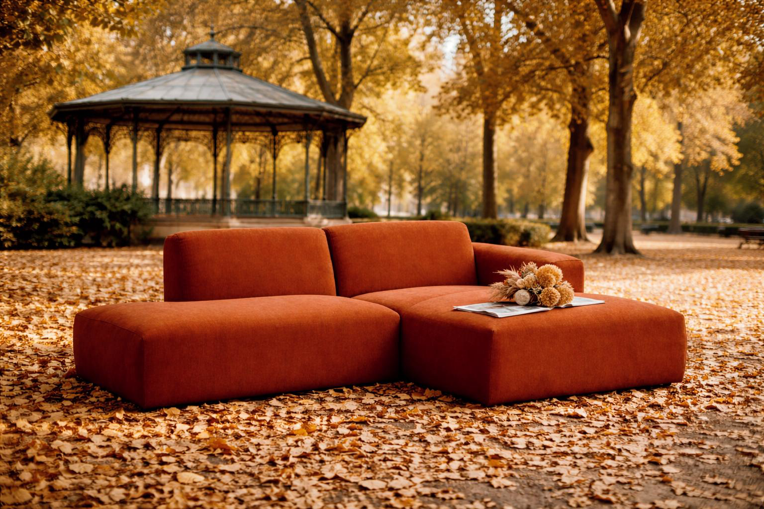 Canapé d’angle Archives Paname Avenue, Collection Arts & Métiers, en tissu chenille marron, installé dans un jardin public parisien en automne, posé sur un tapis de feuilles avec kiosque en arrière-plan, bouquet de fleurs séchées et journal sur l’assise.