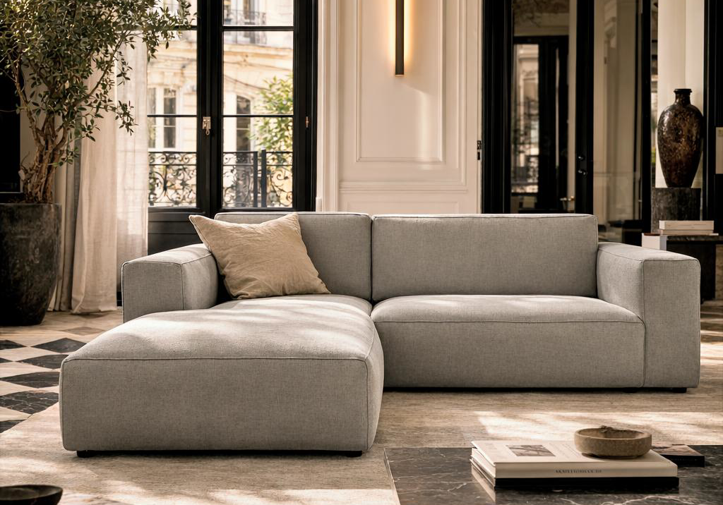 Canapé d’angle gauche Roi de Sicile Paname Avenue en tissu chenille gris dans un intérieur parisien élégant avec grandes fenêtres, moulures, parquet et ambiance lumineuse haut de gamme