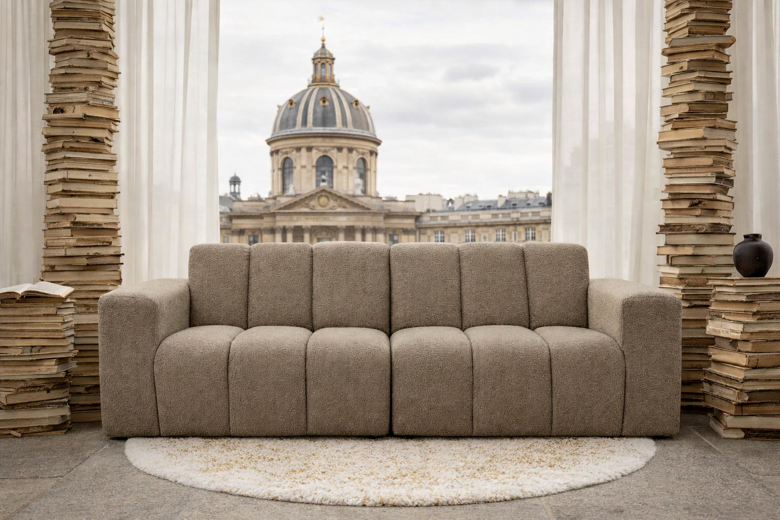 Canapé Mazarine dans un décor onirique parisien constitué d'une pile énorme de livres de part et d'autres du canapé qui est face à la fenêtre donnant sur l'Eglise adjacente à la rue