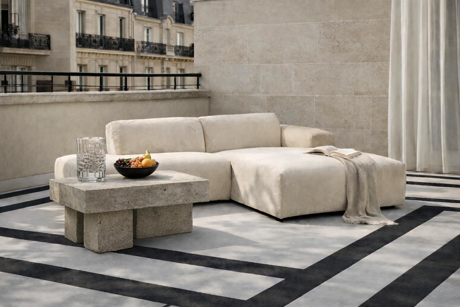 Canapé d'angle Temple Paname Avenue installé sur une terrasse parisienne avec table basse en pierre, fruits et livre, dans une ambiance extérieure élégante et lumineuse.