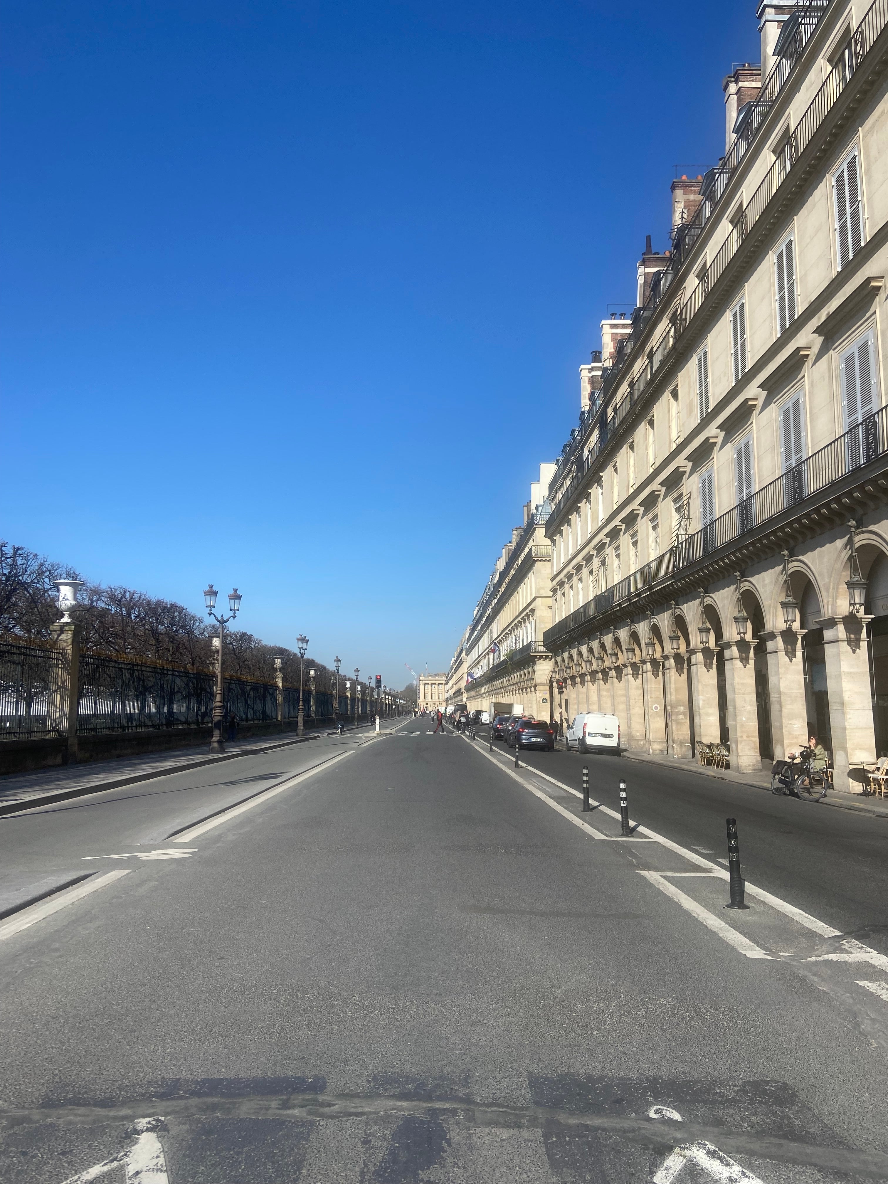 Vue perspective des arcades haussmanniennes de la rue de Rivoli sous un ciel bleu, décor emblématique de la marque Paname Avenue à Paris.