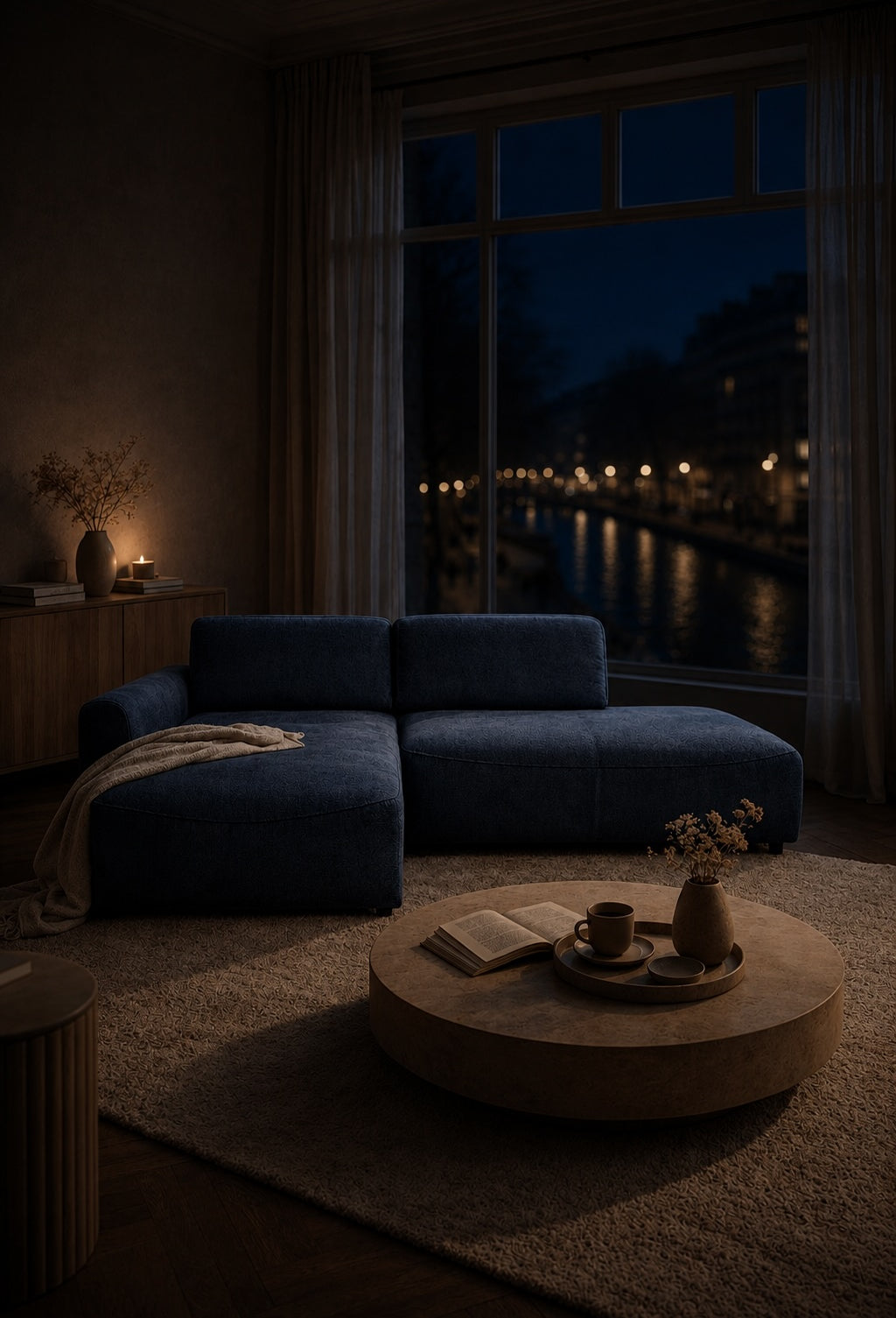 Canapé d'angle Château d'Eau en tissu chenille bleu dans un salon contemporain avec table basse ronde effet pierre, vue sur canal illuminé et ambiance nocturne