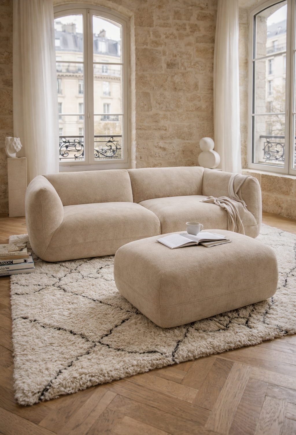 Canapé Portefoin et pouf Blainville sur un tapis berbère dans un décor d'intérieur parisien avec murs en pierre et parquet en point de Hongrie.