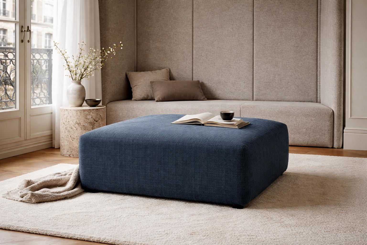 Pouf Albert Thomas Paname Avenue en tissu chenille bleu utilisé comme table basse dans un salon lumineux avec parquet, tapis clair et décoration minimaliste élégante