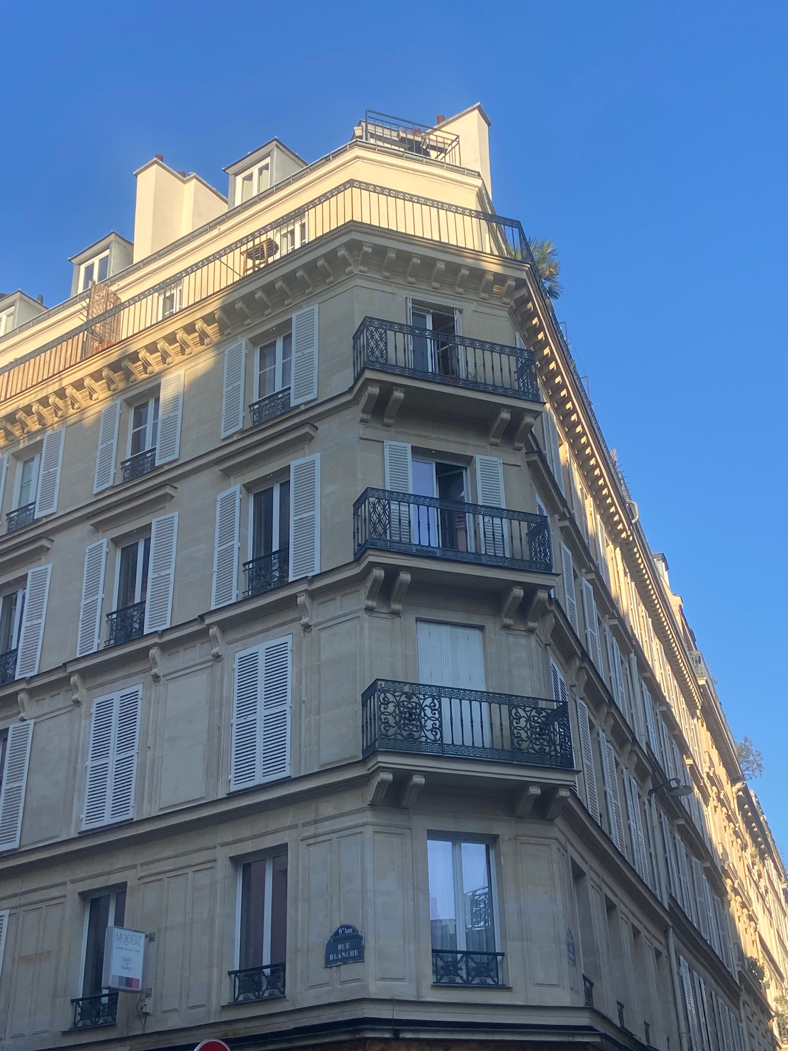 Immeuble haussmannien d’angle rue Blanche à Pigalle Paris 9 avec balcons en fer forgé et façade typique parisienne sous ciel bleu