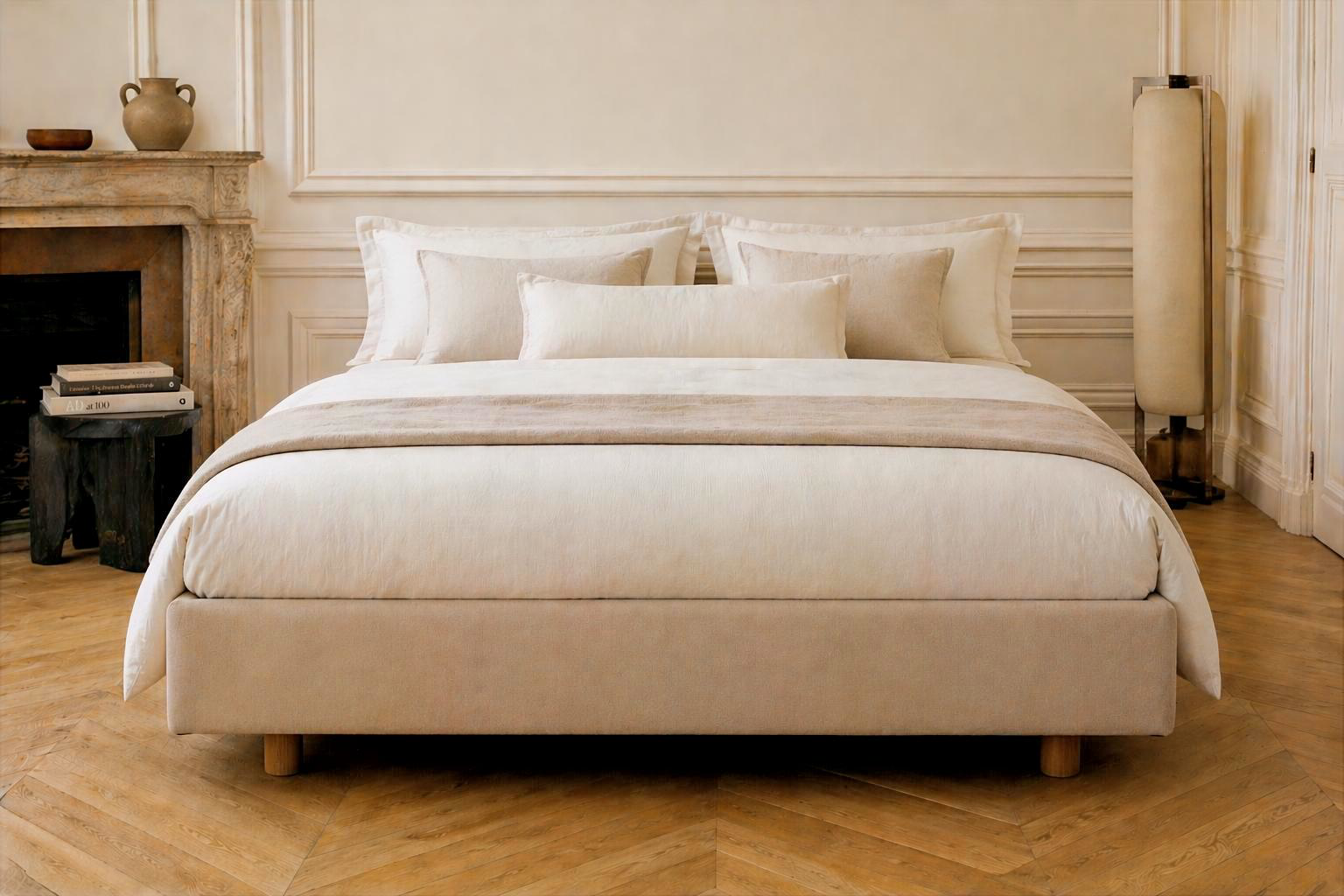 Sommier tapissier Richard Lenoir 140x200cm habillé de linge de lit en lin beige et blanc, dans une chambre avec cheminée ancienne et parquet point de Hongrie.